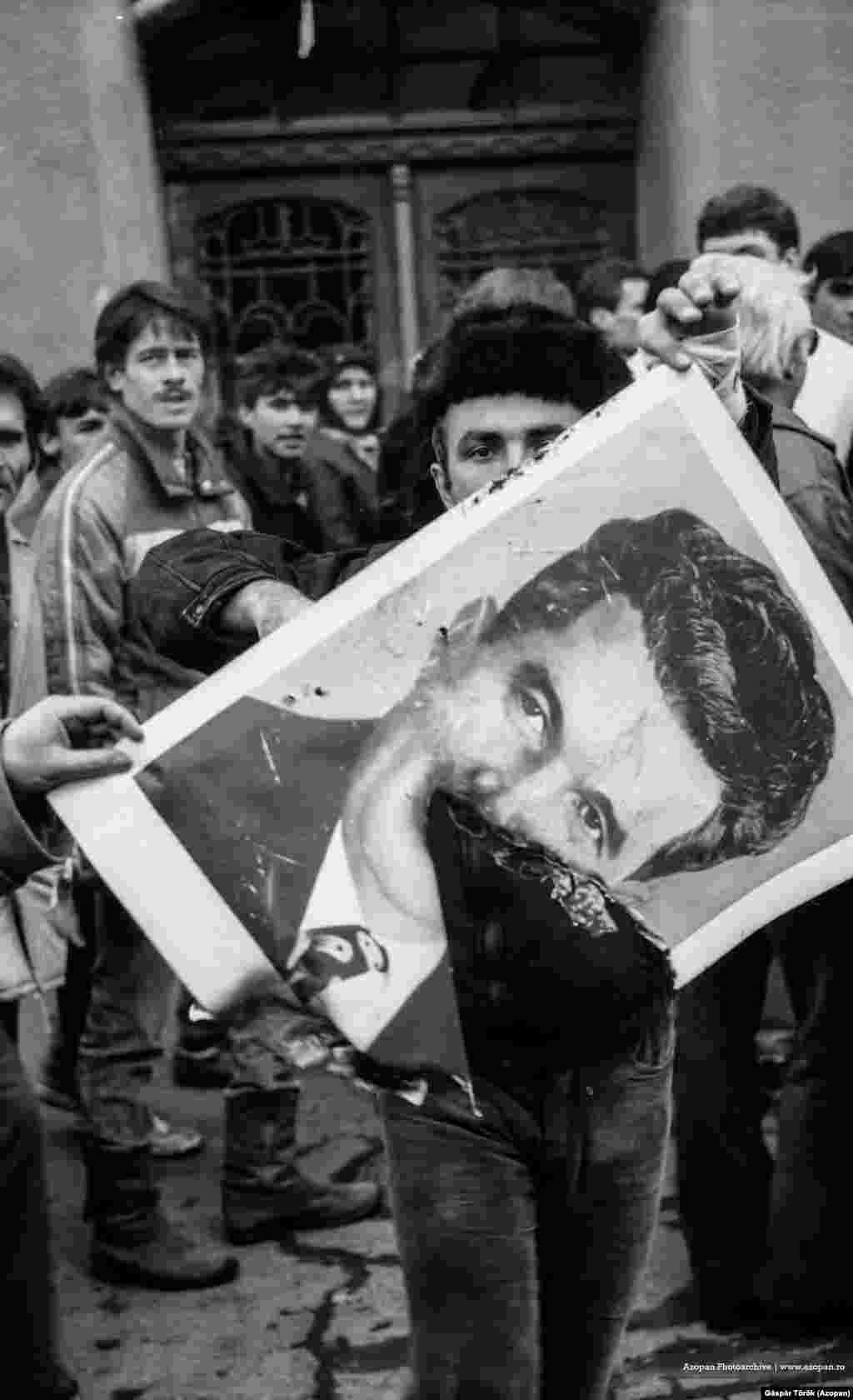 Un bărbat flutură un portret parțial ars cu Ceaușescu, în Târgu Mureș, pe 22 decembrie 1989, în timpul revoluției care i-a scăpat pe români de disprețuitul dictator. 